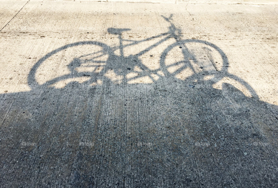 Shadow of a bicycle placed on top of the car and being taken to pedal on the beach.