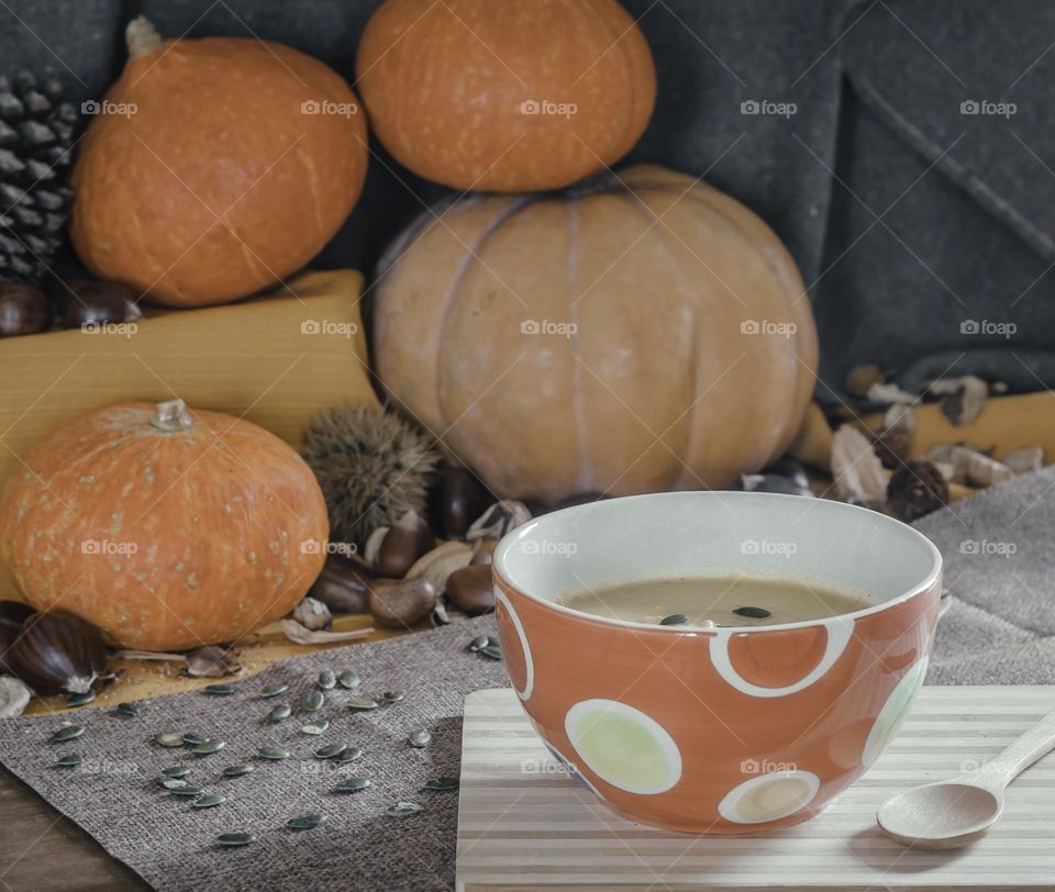 A bowl of cream of pumpkin soup against a background of autumnal ingredients 