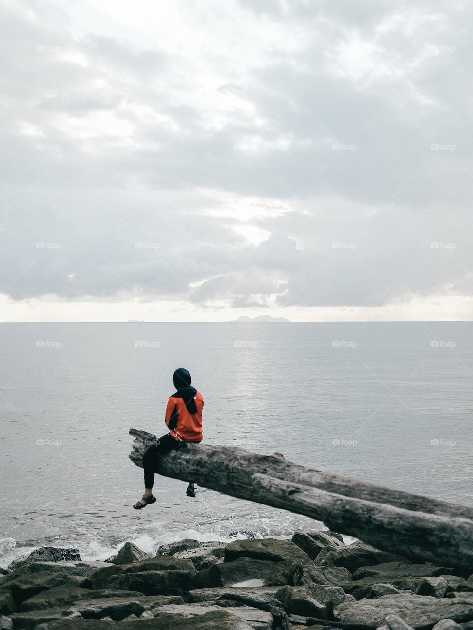 A girl sitting a drift wood by the ocean pondering about the future