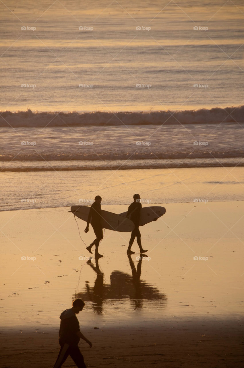 Two surfers walk the beach with their surfboards in California at
