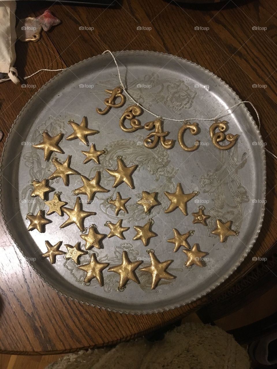 Antique pewter platter with gold painted salt dough Christmas ornament stars and a garland that spells out “Peace”