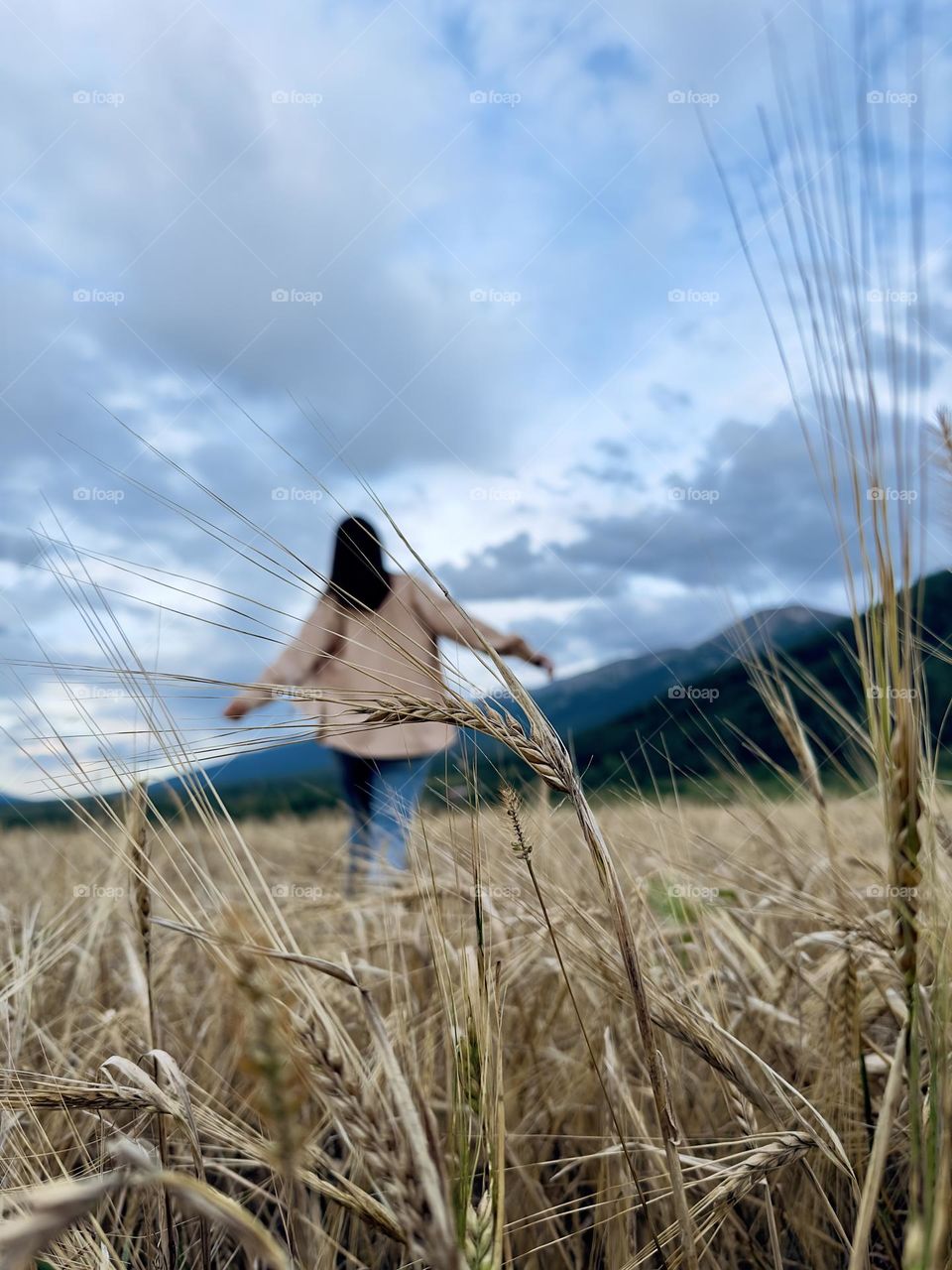 a girl in a beige shirt walks through a wheat field