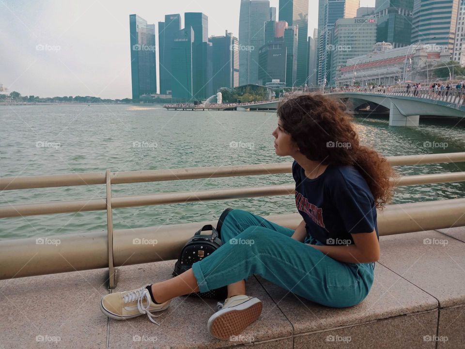 The effect of waters on a busy city, girl sit by a rail in Singapore