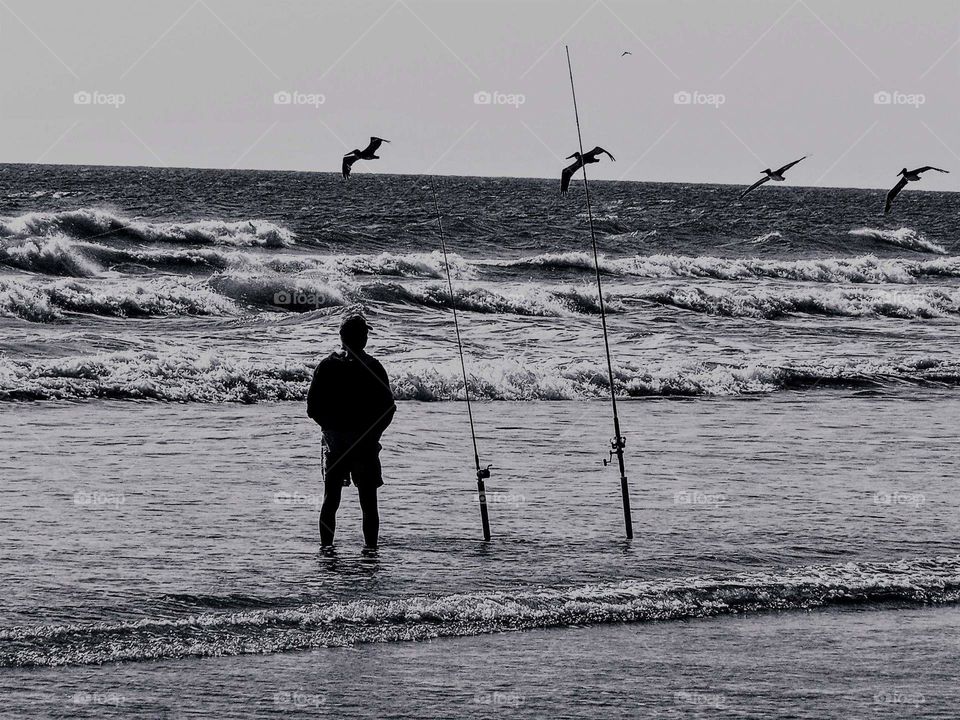 world black and white fisherman with pelican flying overhead on Pawleys Island SC beach