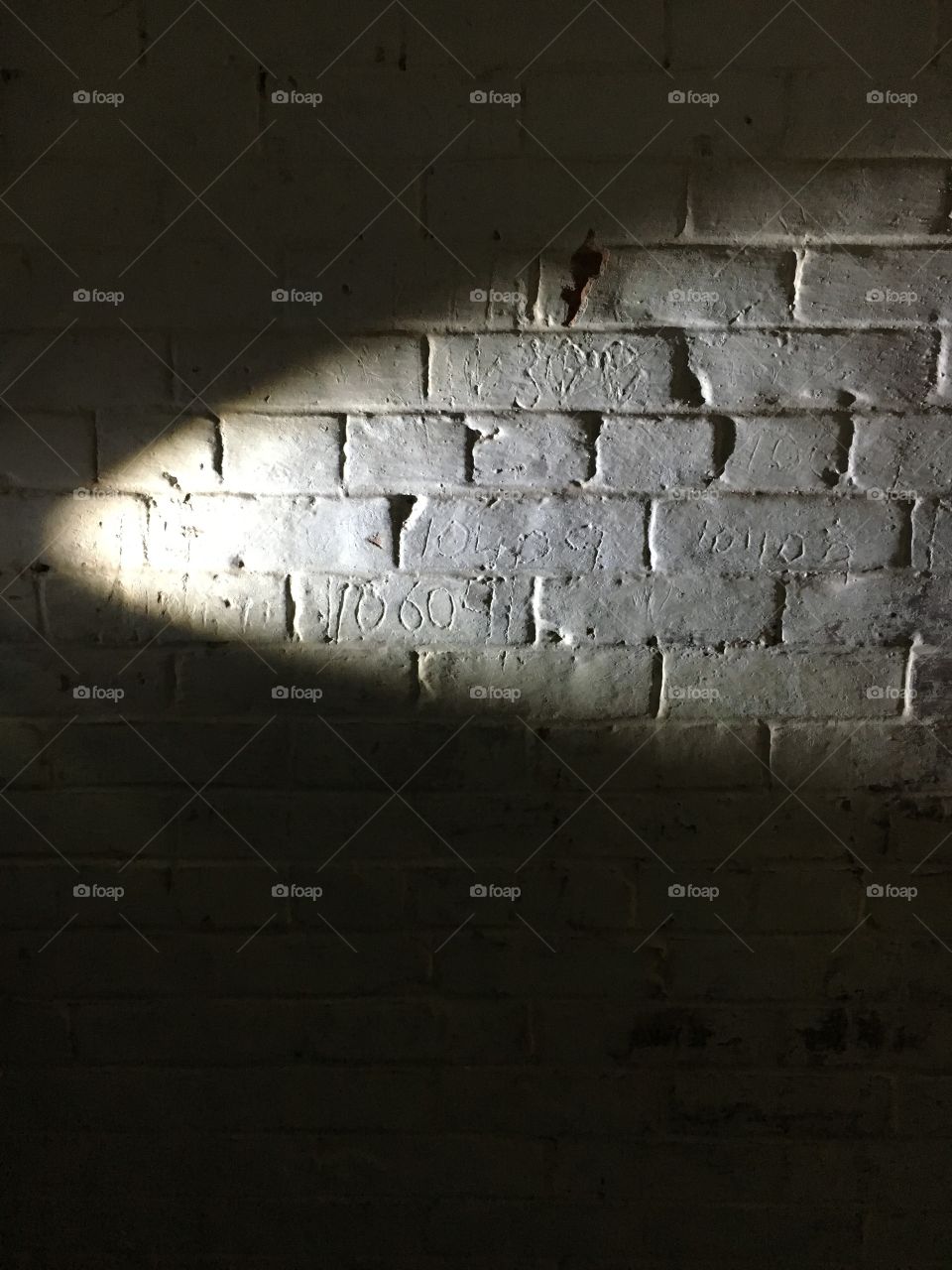 Gray brick wall with a light source. Some bricks have numbers etched into them. 