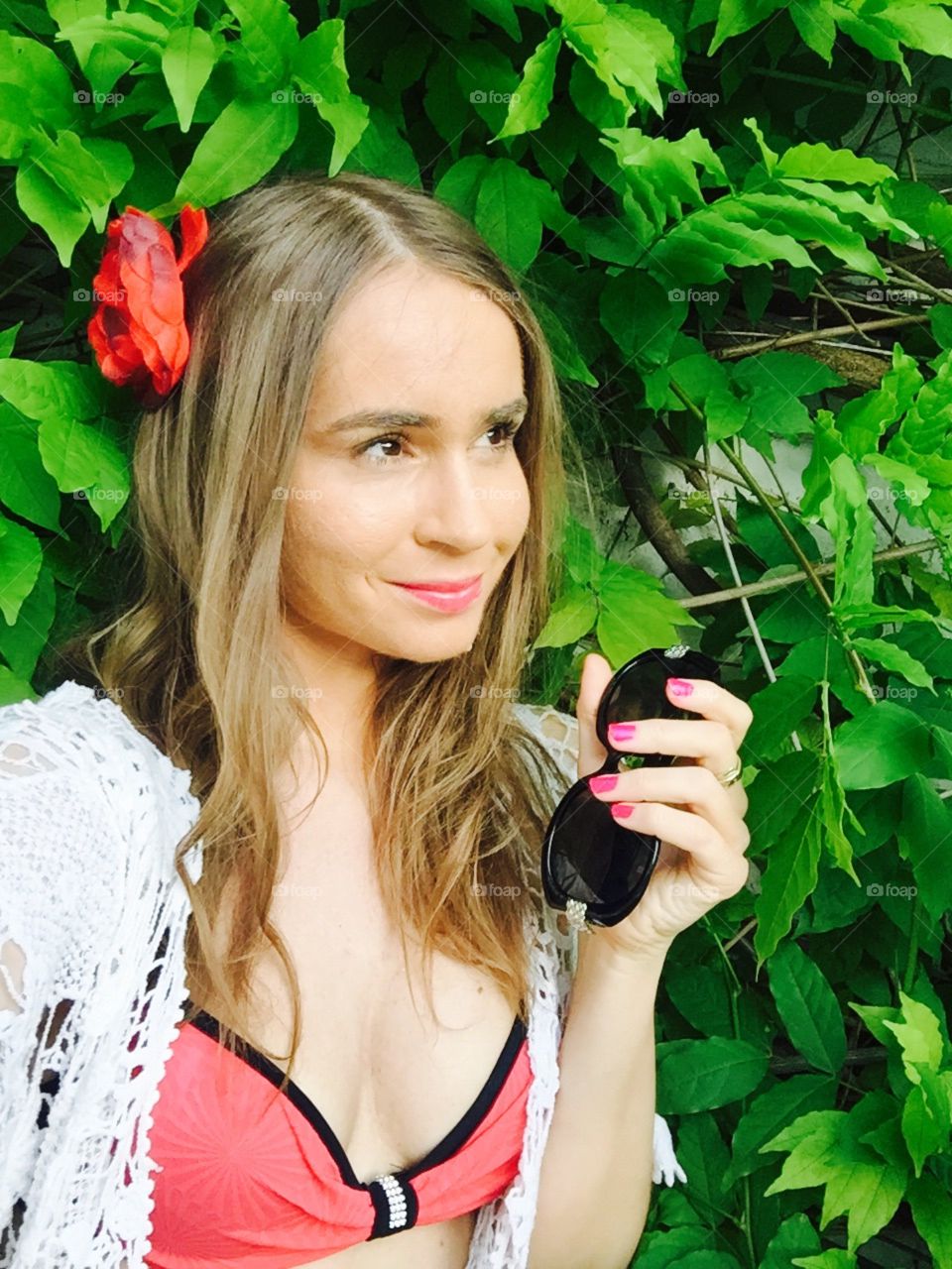 Selfie of woman with long dark blonde hair with black sunglasses in her hand standing against background made of leaves