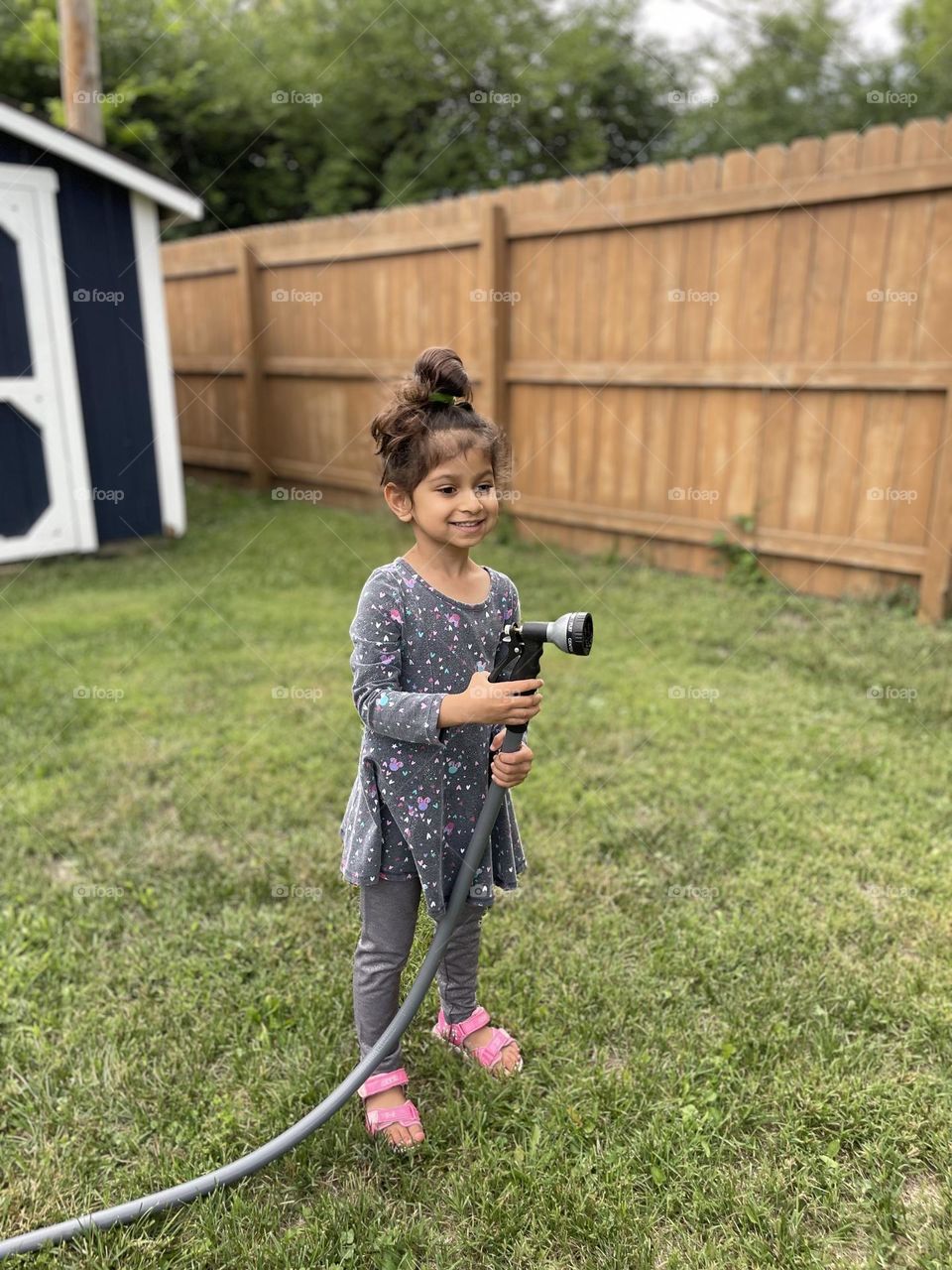 Little girl helps mommy in the backyard, mommy and me time, watering the garden with the hose