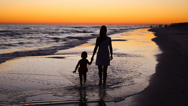 Silhouette of mother and daughter walking on beach
