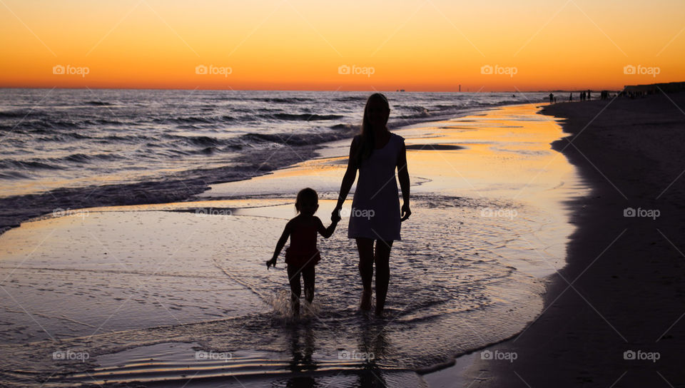 Silhouette of mother and daughter walking on beach