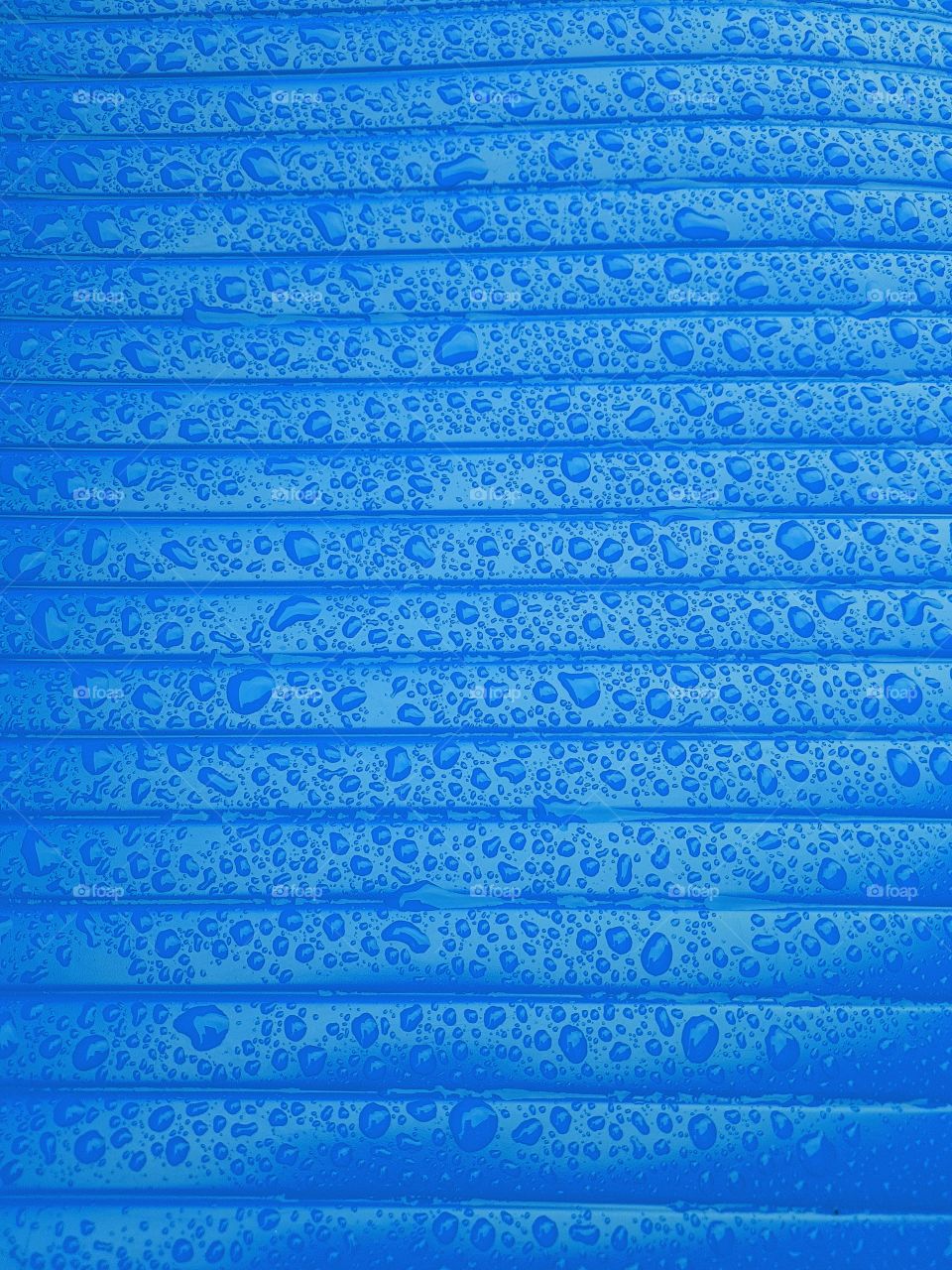 Close up of water droplets on a wet shiny plastic surface blue with horizontale lines parallele