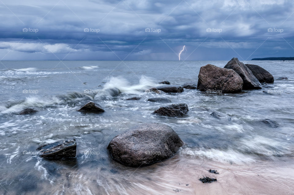 Seascape. Storm clouds gathering over the rocky beach. There is lightning in the distance.