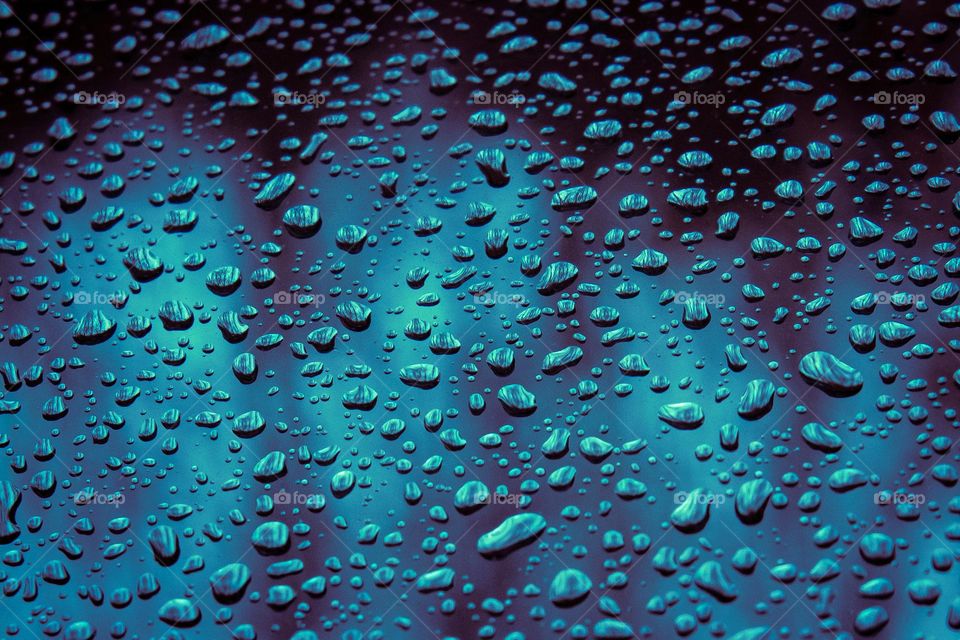 Deeply blue rain drops on glass. Tons of tiny rain droplets on a car windshield during a rainy day in New England.