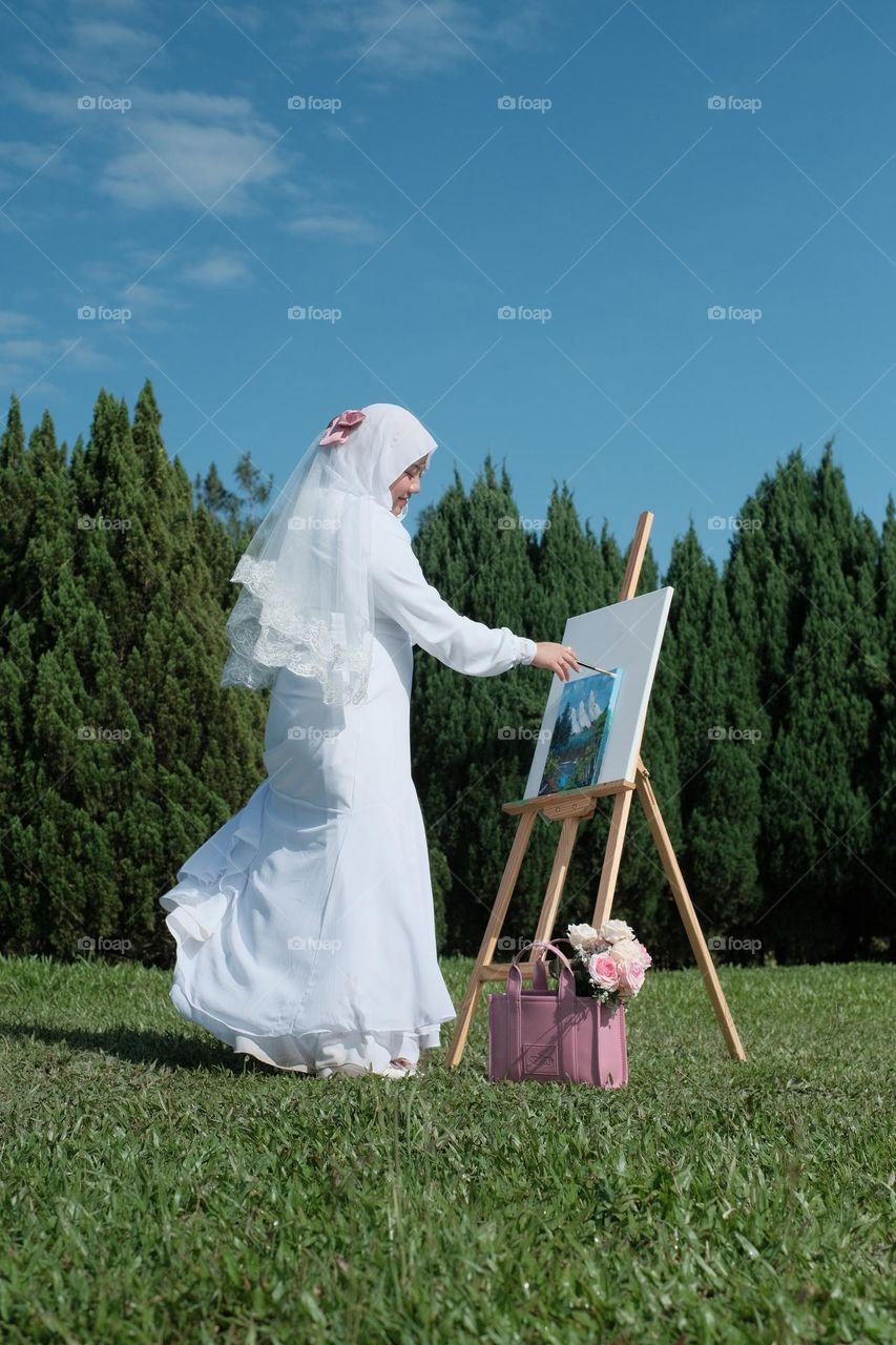 a girl wearing white dress drawing during summer time.