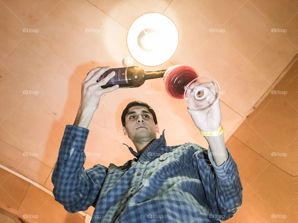 Standing man pours wine into wine glass, shot from floor 