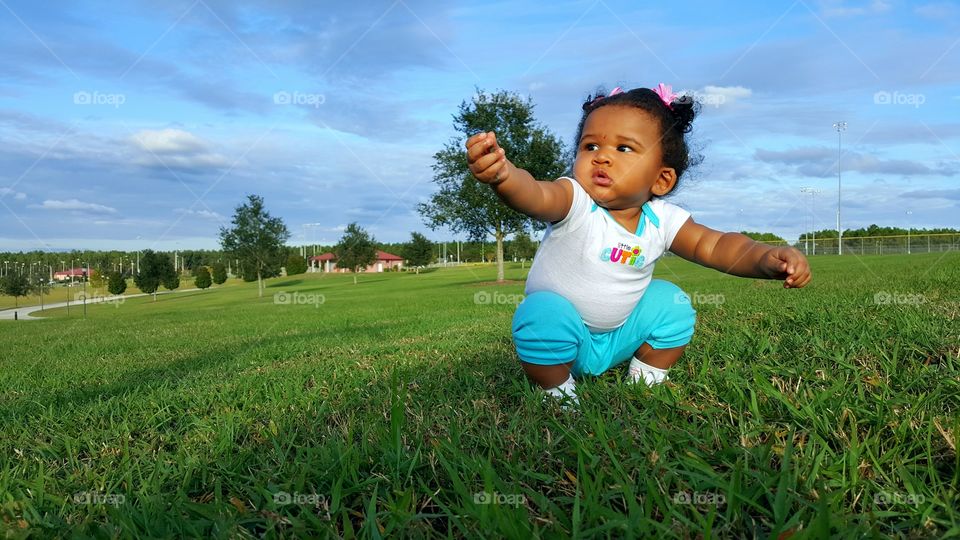 A little toddler girl sitting on grass at countryside