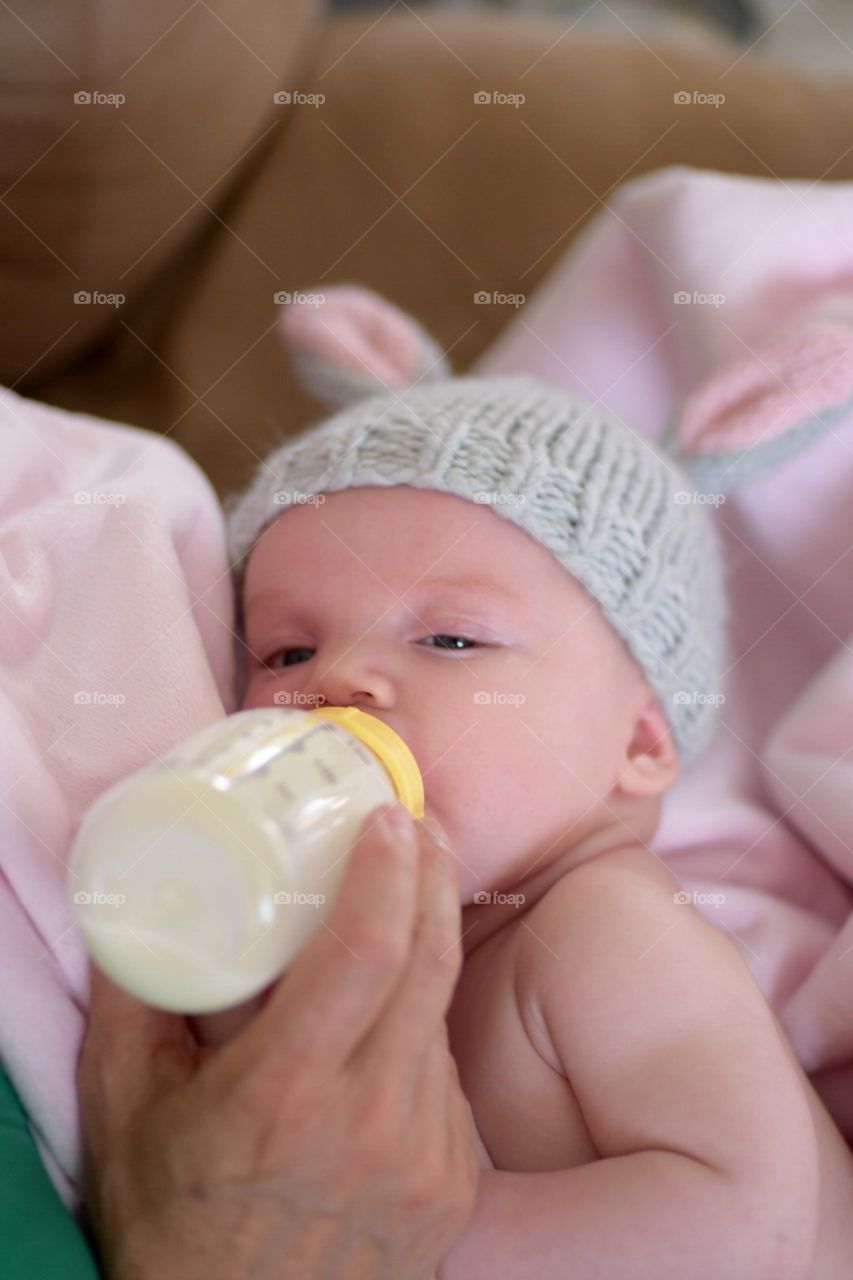 Newborn baby wearing Easter bunny ears and drinking from a bottle while being cradled by mother