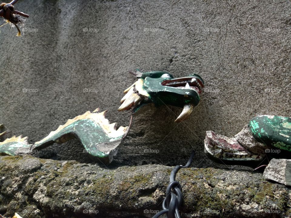 a garden dragon figurine lay in ruin due to neglect and old age. Despite the visible damage, he sat there alone, as if struggling to rise up, looking towards the heaven above.