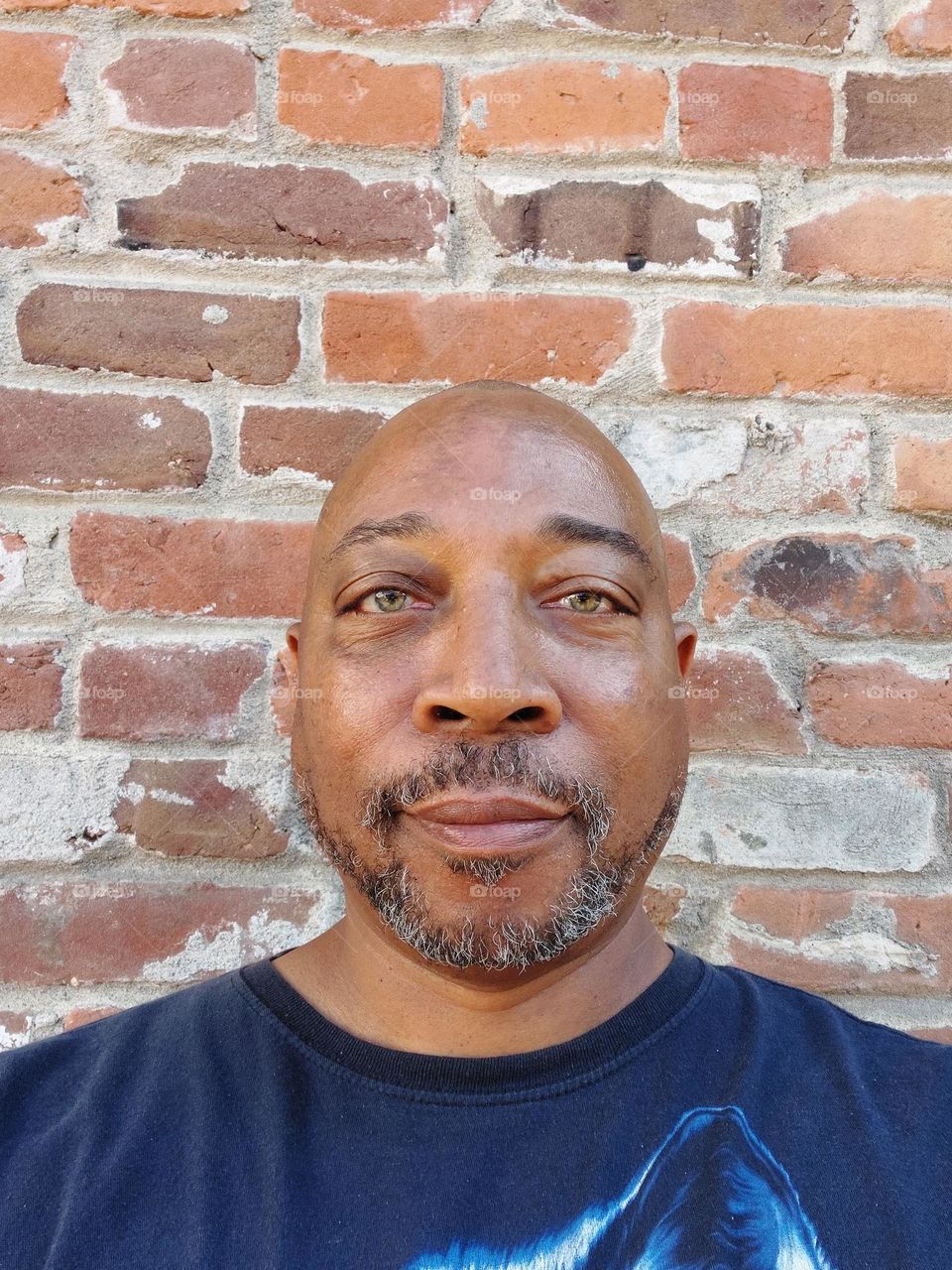 Portrait of a man with a bald head and a Gray beard with red brick wall in the background