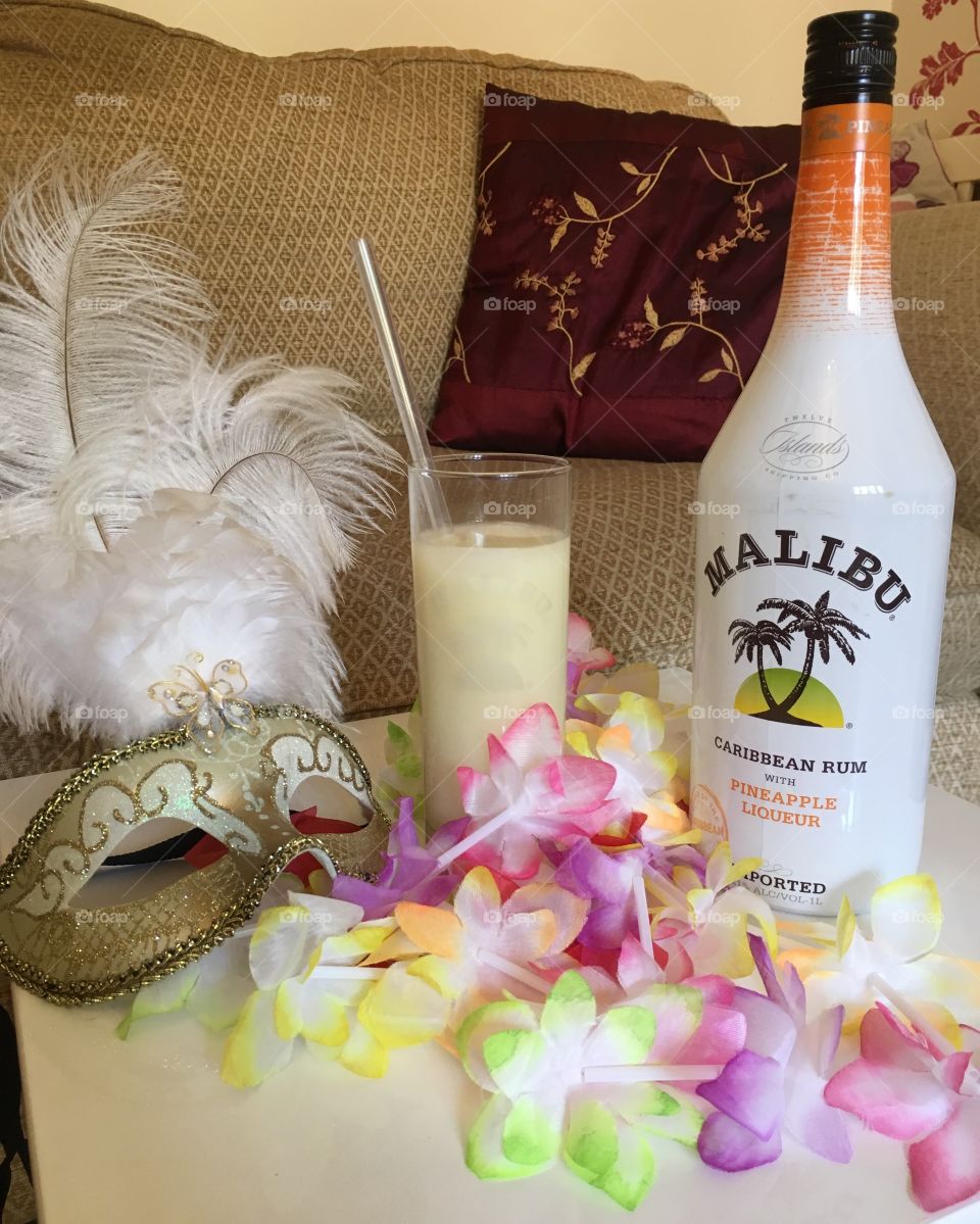 Venetian masquerade mask with a pina colada drink and a bottle of pineapple flavoured Malibu and flower garlands 