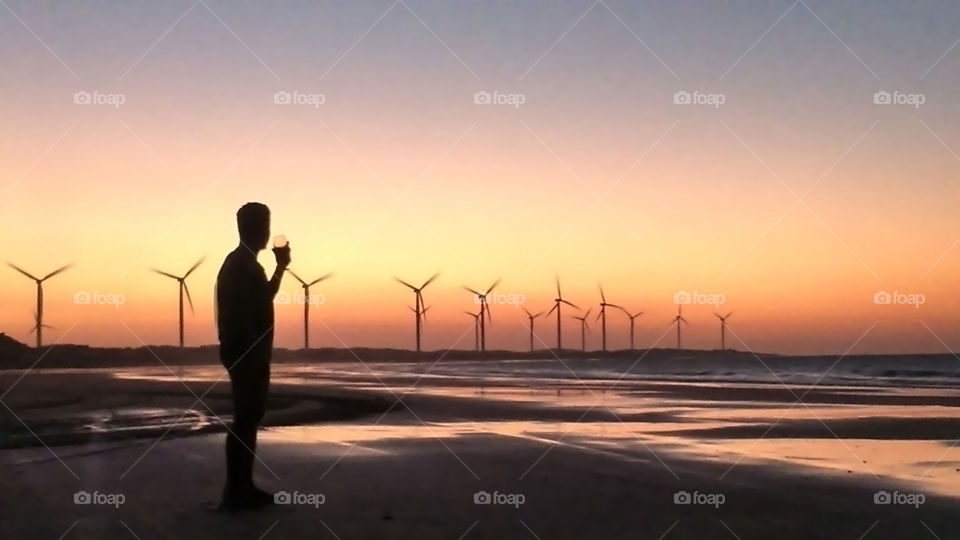 Man with wine glass watching sunset with wind turbines
