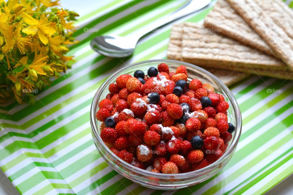 wild strawberries and blueberries on a plate tasty healthy food and yellow flowers, summer time