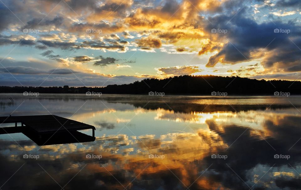 amazing sunrise over the lake in poland with pier and forest silhouette