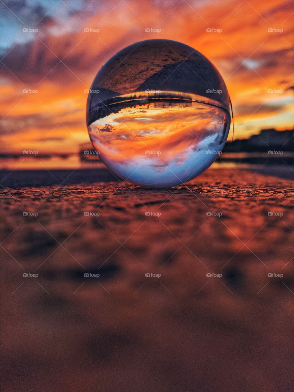 Beautiful reflection of the bright red sunset sky in lens ball or crystal ball close up. Summer vacation time.