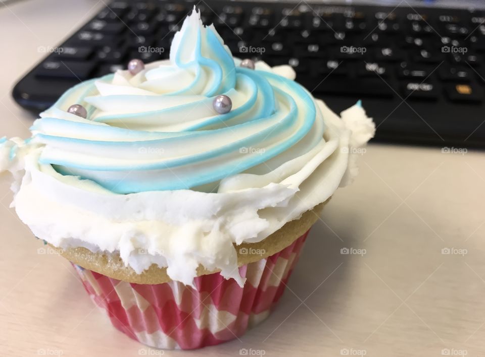 Blue and white swirl frosting Crazy cupcake snacking at the office conceptual photography with computer keyboard in background 