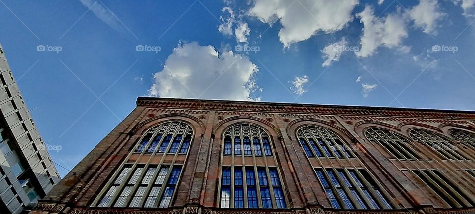 This large brownstone building w arches extending over several floors enclosing tall partitioned windows looks like it could be found in “Williamsburg”, Bklyn. It is actually located in “Munich”, the capitol of “Bavaria”. 2022. Hypnotic Productions