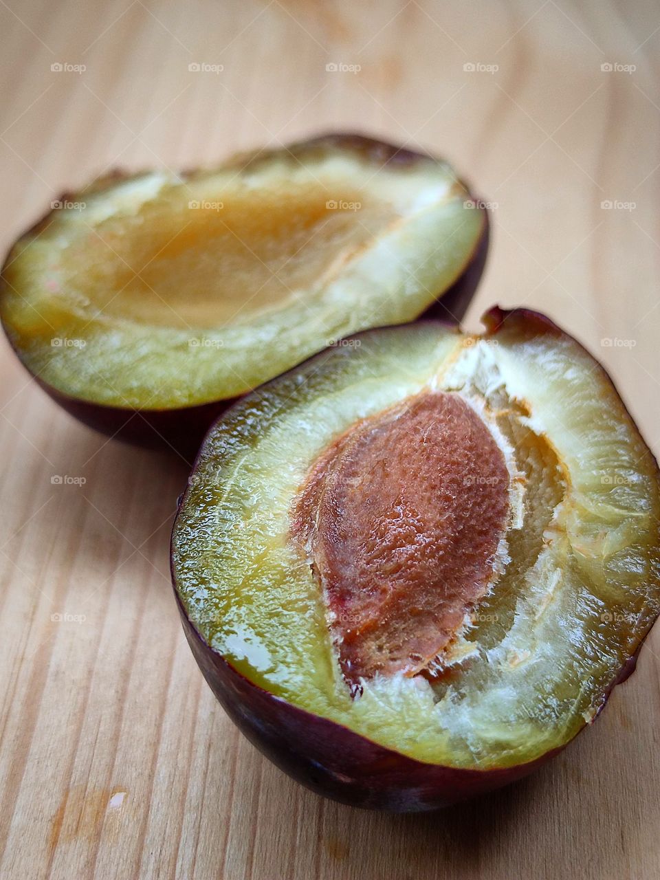 A plum that is split into two halves. There is a in one half has berry seed