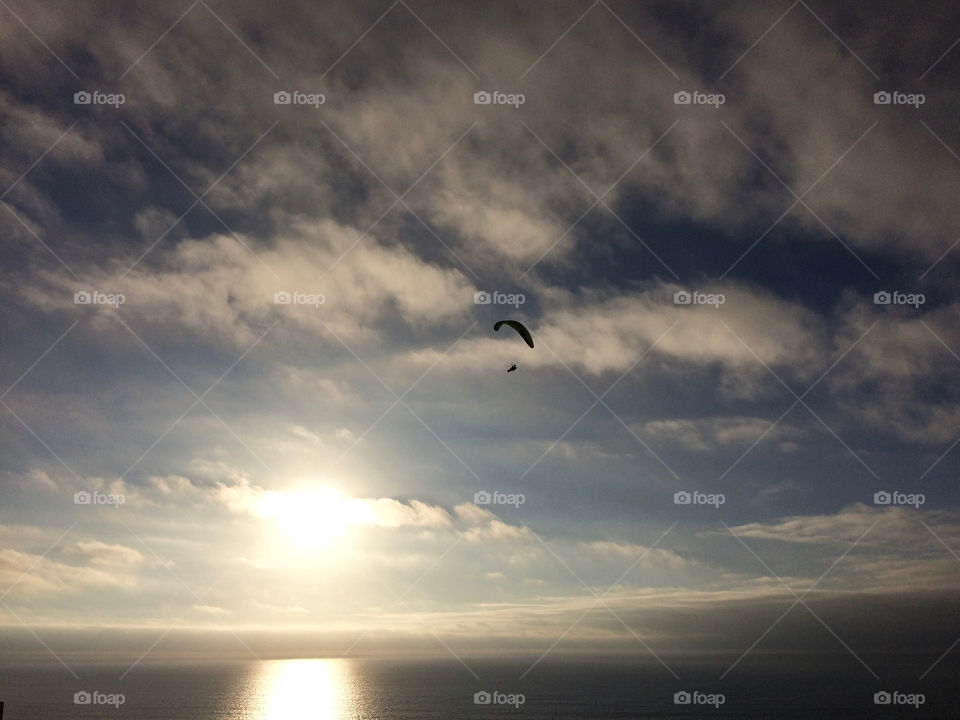 Lone paraglider floating into the setting sun, over the cliffs of Torrey Pines