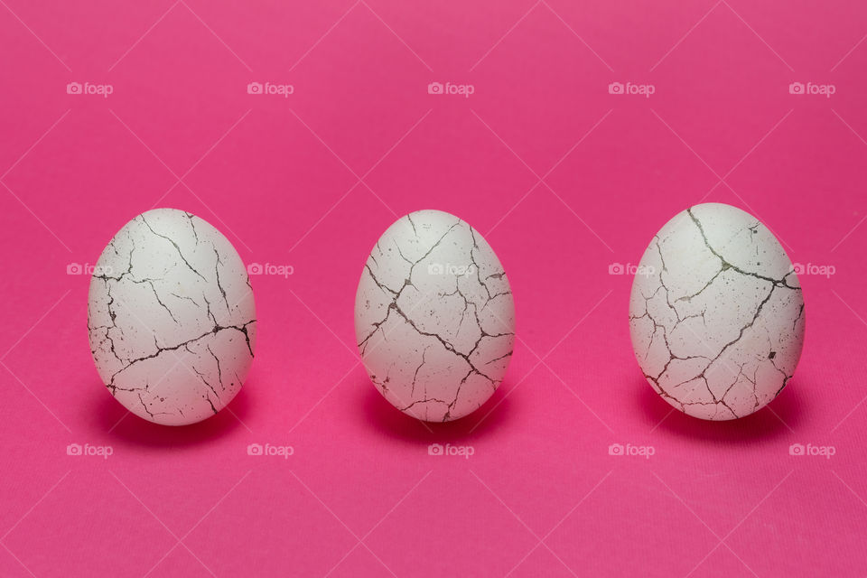Three white organic eggs on pink background. Cracked like paint