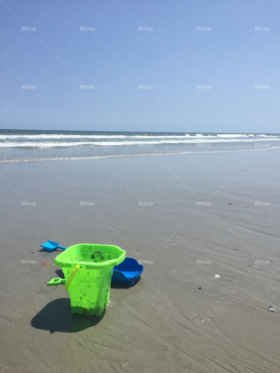 Beach scene. A child's sand bucket sits on the sand by the seashore