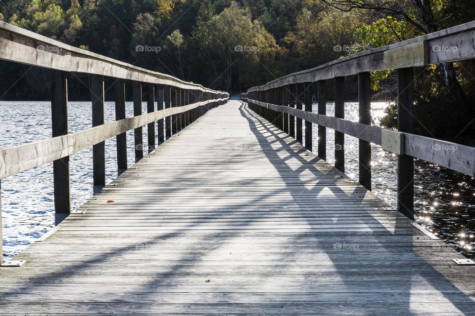 Long wooden pier with shadows crossing the lake water on a sunny day 