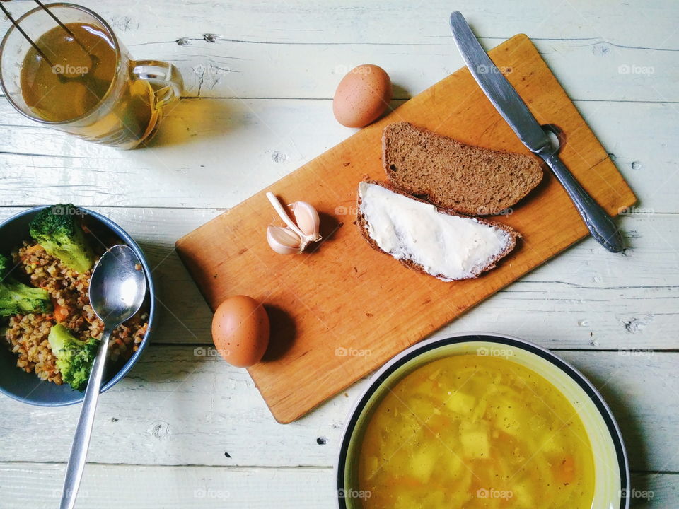 vegetable soup, a bowl of buckwheat porridge, bread and butter, eggs, a cup of tea and garlic on the table