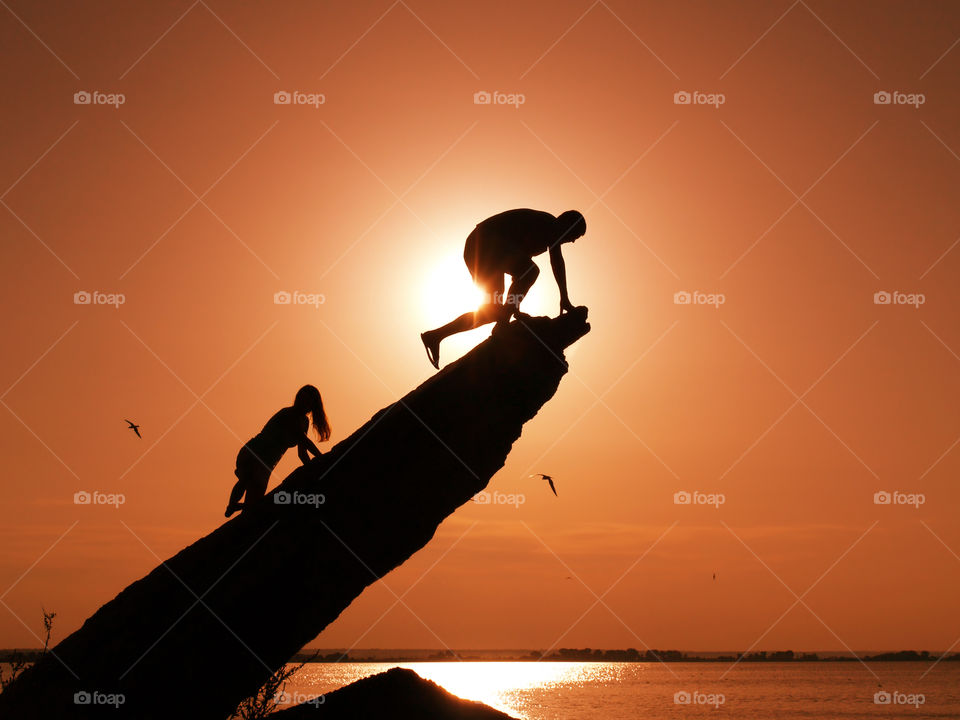 Two silhouettes on the rocks, sunset background