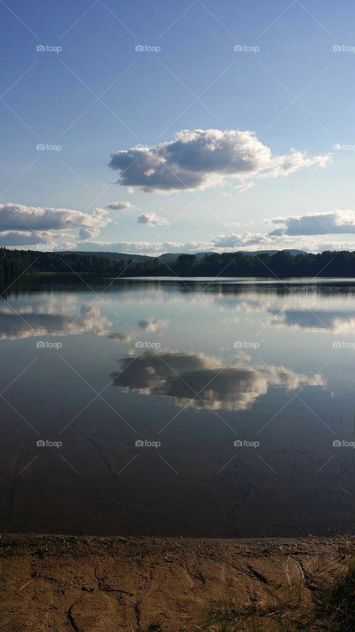 Clouds reflecting over a  lake during a  summer afternoon with a bit of sandy beach