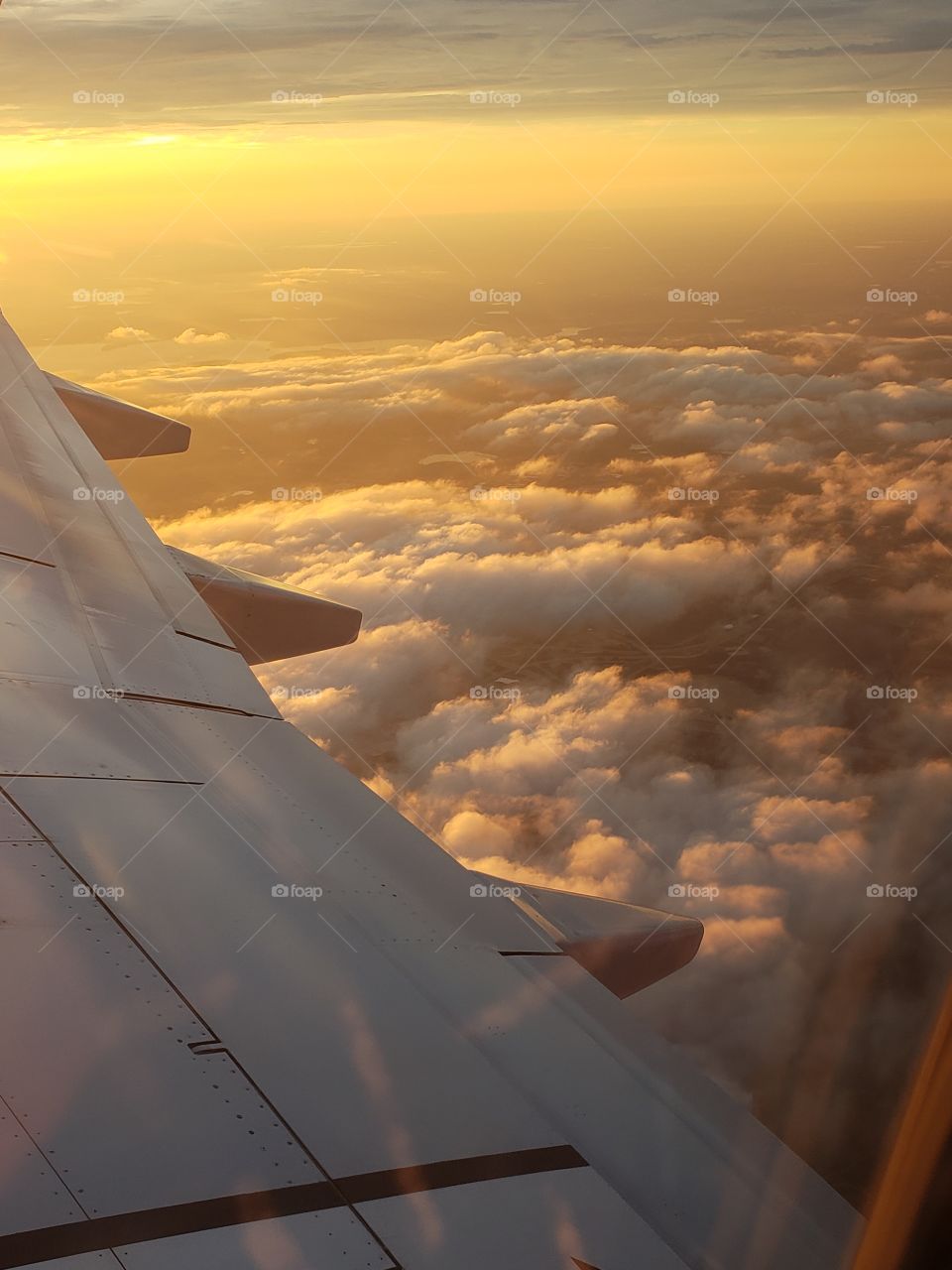 Sunset from 30,000 in the air. Airplane soars above clouds in an orange sunset.