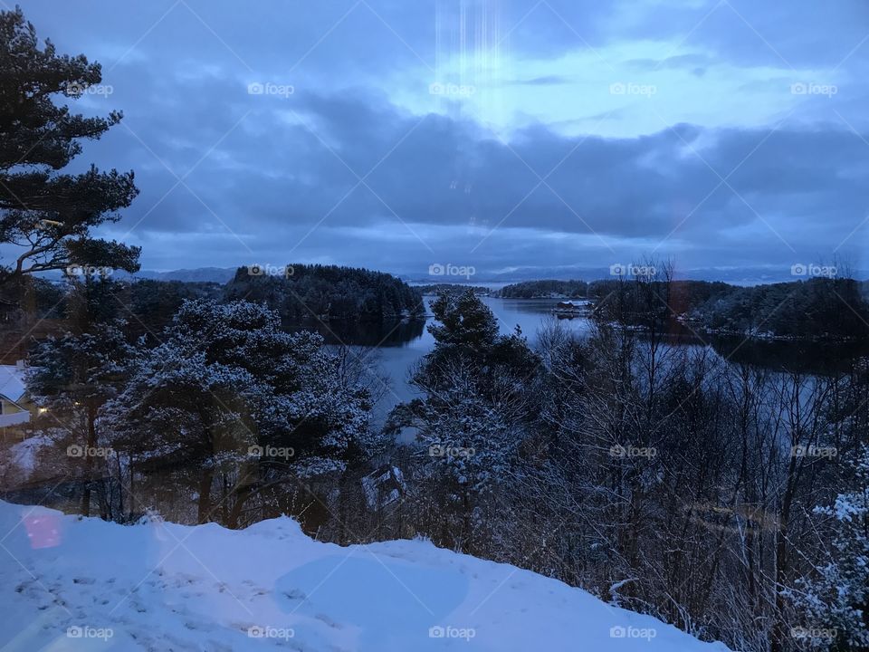 The evening is falling in the white winter in Norway. There is still some snow left, but some have already melted away. There is a really nice view out to the fjord. There is some reflections in the picture, which in my opinion makes it look cool.