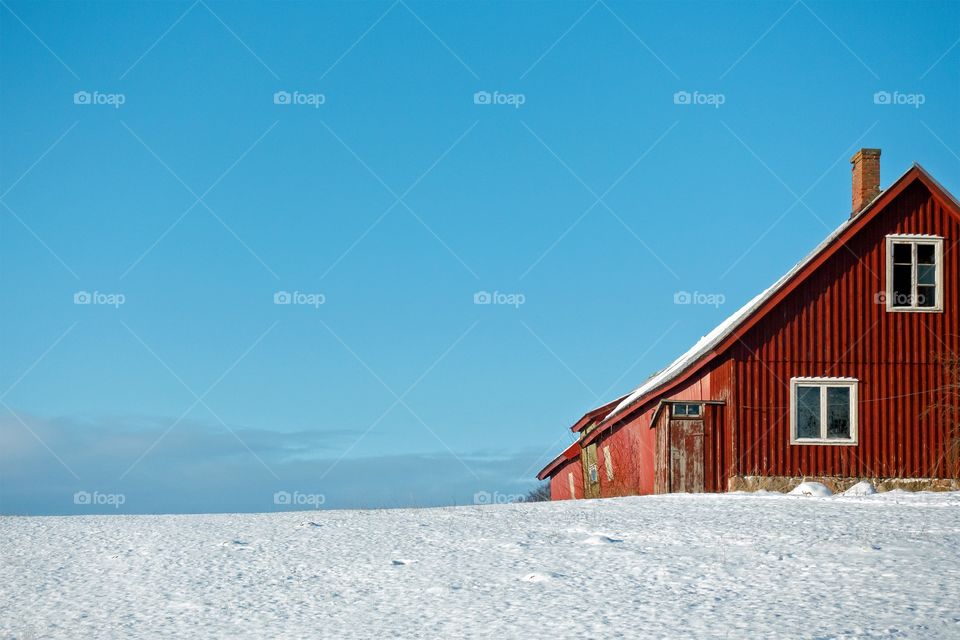 Red, woden house on a hill with snow and blue sky