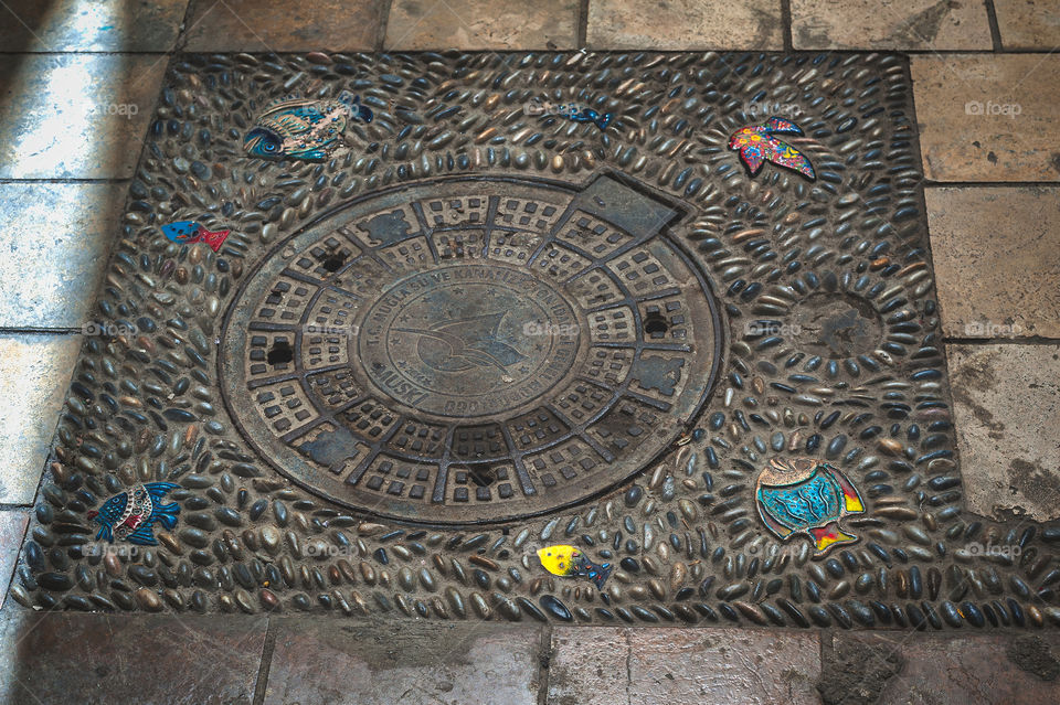 Decorated manhole with pebbles and colorful ceramics fish and bird.