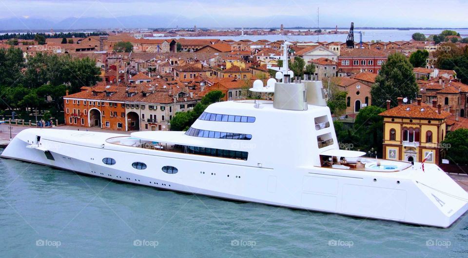 A white mega yacht moored along one of the islands of Venice, Italy on a rainy autumn afternoon
