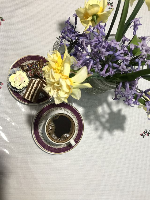 Cup of coffee with black turkish coffee on the table beside narcissus and hyacinth flowers and cookies on a small plate.