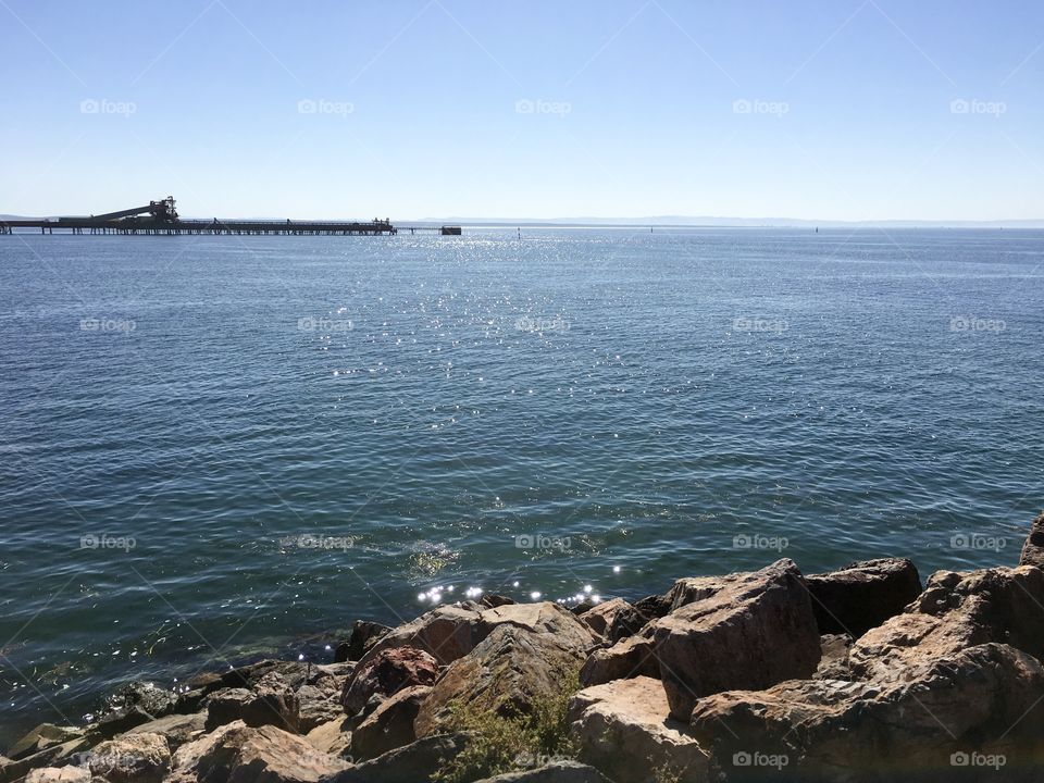 Sparkling sea with industrial steel mill loading dock in distance