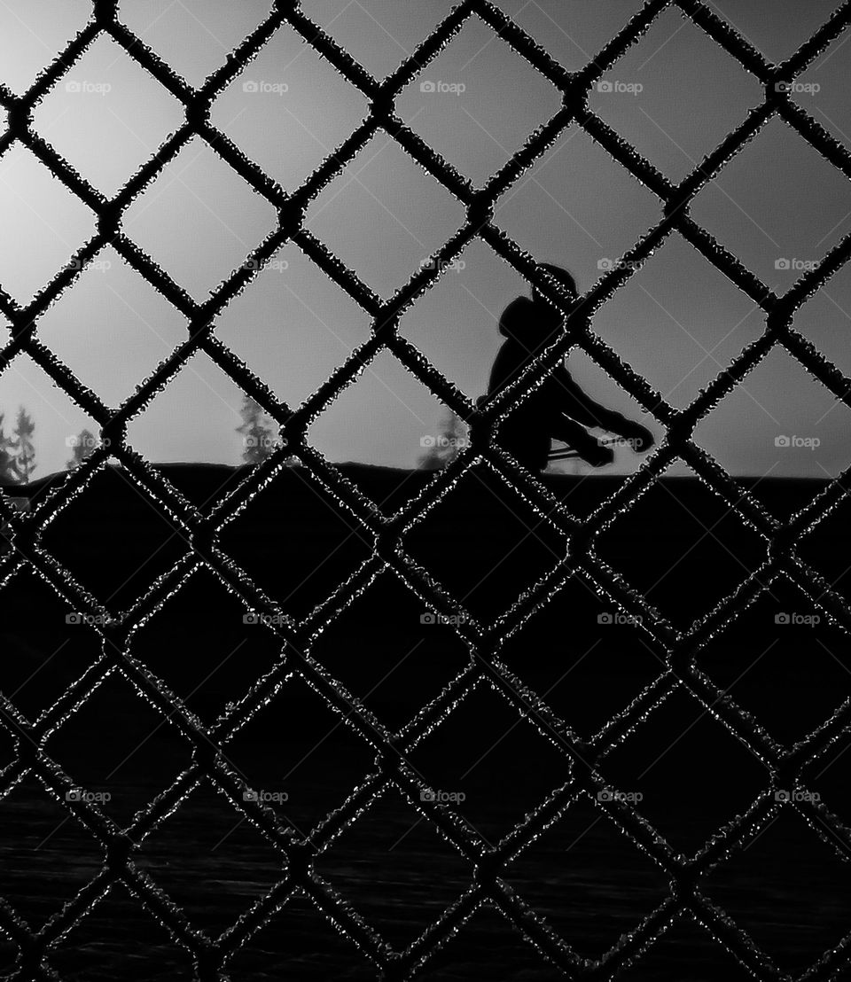 The Man outside the fence .
the silouetts of a man skeeing outside the fence. The light from the sun makes rare light .