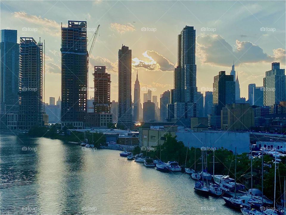 Against the golden light of the evening sun the skyscrapers that make up this magnificent city old, new or under construction can be seen like tall dark silhouettes. A golden glow passes between the waters above and below. 2023. Hypnotic Productions