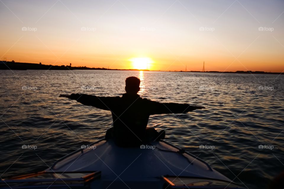 Young man on a boat. Free as a bird he glides towards the sun on a wonderful summer evening