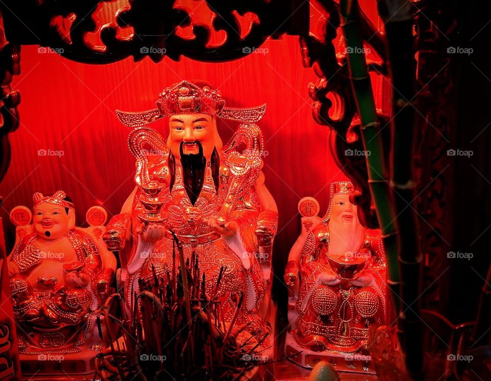 Happiness. Home Buddhist temple. Three smiling figurines among green bamboo and scented candles. In the center is a statue of Tsai Shei, the god of wealth.