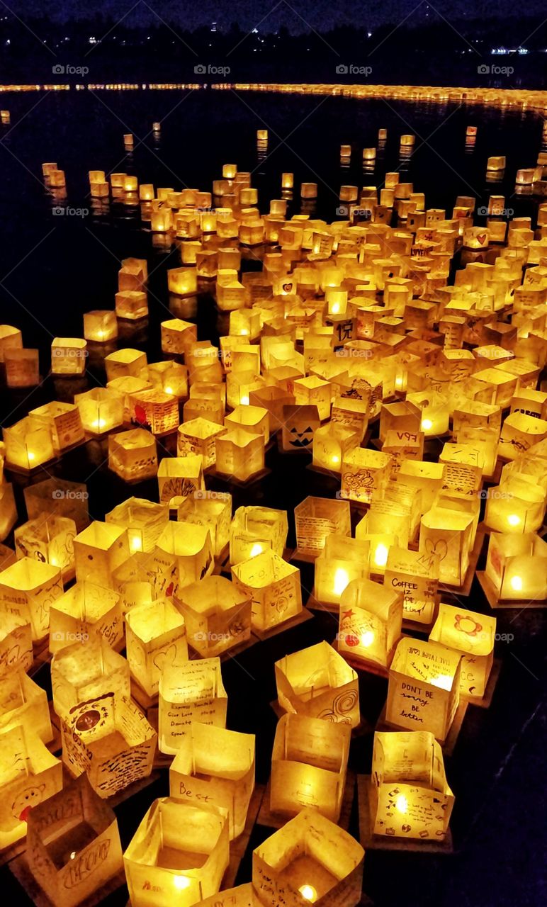 Hundreds of beautiful lighted lamps with written messages or hand drawn artwork floating during a water lantern festival held at night on a lake.