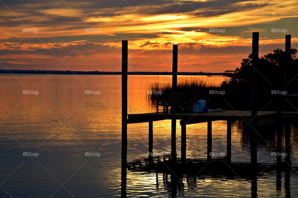 Multiverse - A spectacular and colorful sunset over a silhouette fishing dock with colorful clouds reflecting in the bay. 